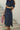 Vestido comprido denim Silvina Campos azul com decote em V, mangas curtas e cinto largo em ráfia.