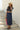 Vestido comprido denim Silvina Campos azul com decote em V, mangas curtas e cinto largo em ráfia.