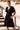 Vestido curto preto da marca Scusi com decote em V e manga fluida, usado por modelo em ambiente exterior.